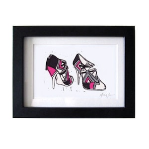 May include: A black framed print of a pair of high-heeled shoes with a geometric pattern in black, white, and pink.