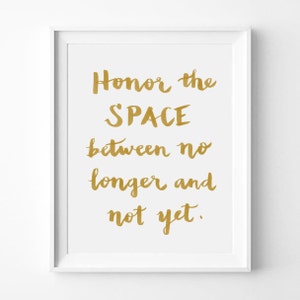 May include: A white framed print with a gold inscription that reads "Honor the SPACE between no longer and not yet."