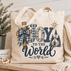 May include: A cream-colored canvas tote bag featuring a blue and white graphic print. The design includes a wooden cross with a blue plaid bow, a church, a star, and the text Joy to the World in blue lettering with a small blue plaid heart.