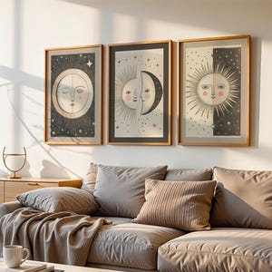 May include: Three framed wall art prints featuring celestial motifs of suns and moons in black, white, and beige. Each rectangular print is encased in a light wood frame, displaying intricate line work and star patterns on a neutral background.