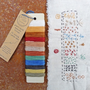 May include: A set of 12 plant-dyed sashiko threads, each 3 yards long. The threads are arranged in a card with a label that reads "plant-dyed sashiko thread 12 colors 3 yards each" and "sustainably dyed by hand with all natural materials katacoida.com".