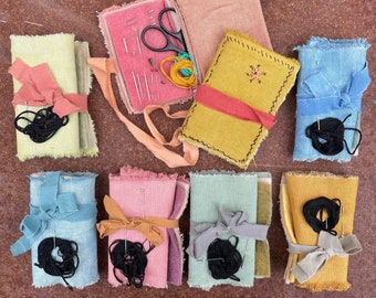 May include: A collection of eight small fabric pouches, some with embroidery, and a pink fabric sewing kit with a small pair of scissors, needles, and thread. The pouches are in various colors, including blue, green, yellow, and brown.