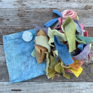 May include: A blue fabric bag with a label that says "Hand-Dyed Wool Felt Scraps" and a pile of colorful wool felt scraps in various shades of blue, green, yellow, orange, pink, and purple.