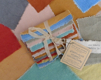 May include: A bundle of 11 plant-dyed fabric swatches in various colors, including blue, green, brown, orange, and yellow. The fabric is organic cotton and hemp. The text on the tag reads: "kata golda handmade 4x4 plant-dyed organic cotton/hemp the beauty fabric is"