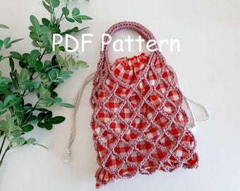 Könnte beinhalten: Eine rosa gehäkelte Netz-Tasche mit rotem und weißem Gingham-Futter. Die Tasche hat einen Kordelverschluss und einen Schlaufe-Griff. Die Tasche befindet sich auf einer weißen Oberfläche mit einer grünen Pflanze im Hintergrund. PDF-Muster.