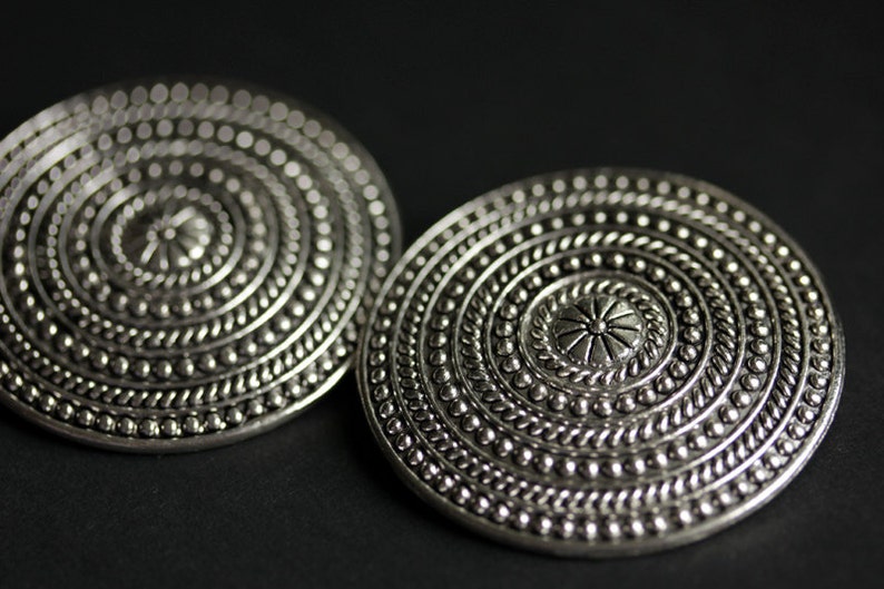 May include: A pair of silver-toned earrings with a circular design featuring concentric circles and a central flower motif.