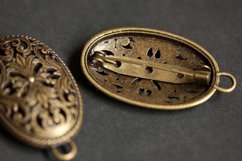 May include: Two antique gold-toned oval brooches with intricate filigree designs. One brooch has a pin closure and the other has a loop closure.