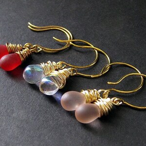 May include: Three pairs of gold wire wrapped earrings with teardrop shaped glass beads. One pair is red, one pair is iridescent, and one pair is pink.