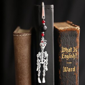 May include: A silver skeleton bookmark with red and black beads hanging from a silver clip. The bookmark is hanging from the spine of a book titled "What Is English? Ward".