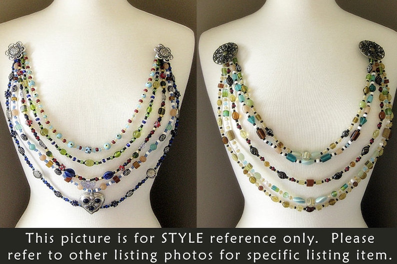 May include: Multi-strand necklace with a heart pendant. The necklace is made of various colored beads, including blue, green, red, and white. The heart pendant is silver with a blue stone in the center.