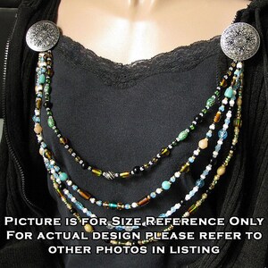 May include: A multi-strand beaded necklace with silver clasps. The necklace features brown, black, white, and blue beads. The necklace is displayed on a black shirt.
