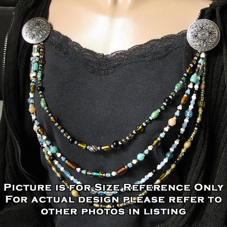 May include: A multi-strand beaded necklace with silver clasps. The necklace features brown, black, white, and blue beads. The necklace is displayed on a black shirt.