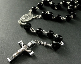 Könnte beinhalten: Eine schwarze Rosenkranz mit einem silbernen Kruzifix und einer silbernen Medaille. Die Perlen sind rund und die Kette ist silber.