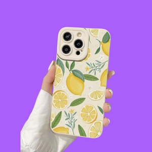 Può includere: Una custodia per telefono con sfondo color crema caratterizzata da un motivo ripetuto di limoni giallo brillante, spicchi di limone, foglie verdi e piccoli fiori bianchi. La custodia presenta un'apertura rialzata e chiara per la fotocamera.