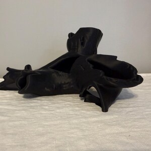 May include: A black, abstract sculpture with a natural, organic form. The piece has a rough texture and appears to be made of a solid material. The sculpture's design features multiple curves and angles, creating a visually interesting piece.