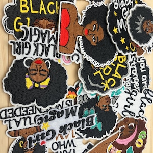 May include: A collection of embroidered patches featuring Black women with natural hairstyles. The patches include text such as "Black Girl Magic" and "I am who I am". The patches are in various shapes and sizes, with black, brown, and white colors.