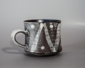 May include: A black and white ceramic mug with a geometric pattern. The mug has a handle and a rounded bottom.