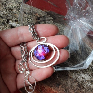 May include: A silver necklace with a purple and red iridescent glass pendant surrounded by three silver rings.