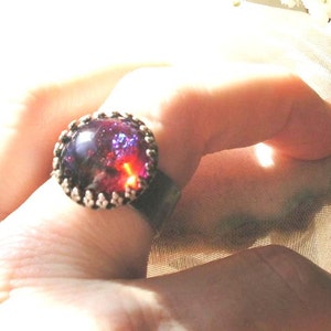 May include: A ring with a large, oval-shaped, purple and red gemstone set in a silver band.