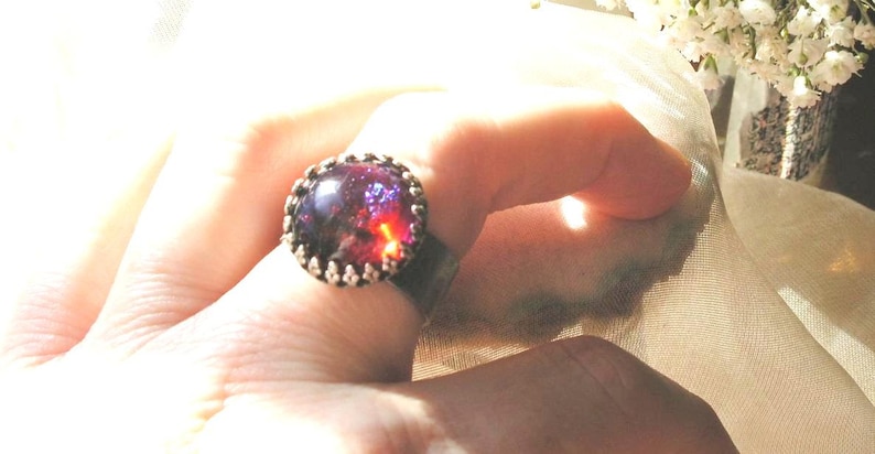 May include: A ring with a large, oval-shaped, purple and red gemstone set in a silver band.