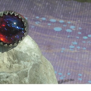May include: A silver ring with a large, round, red and blue opal gemstone.