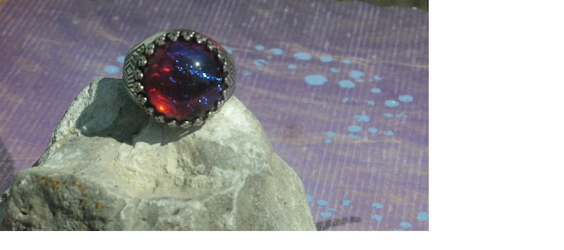 May include: A silver ring with a large, round, red and blue opal gemstone.