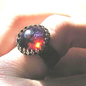 May include: A silver ring with a large, round, dark purple and red gemstone set in a silver bezel.