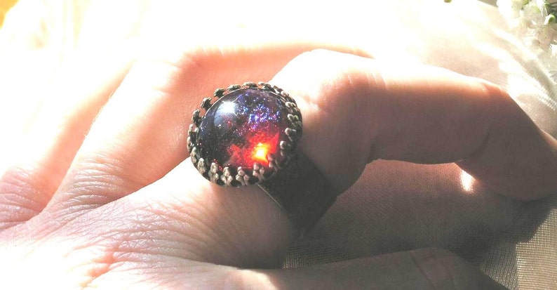 May include: A silver ring with a large, round, dark purple and red gemstone set in a silver bezel.