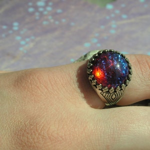 May include: A silver ring with a large, round, red and blue iridescent gemstone set in a detailed silver bezel.