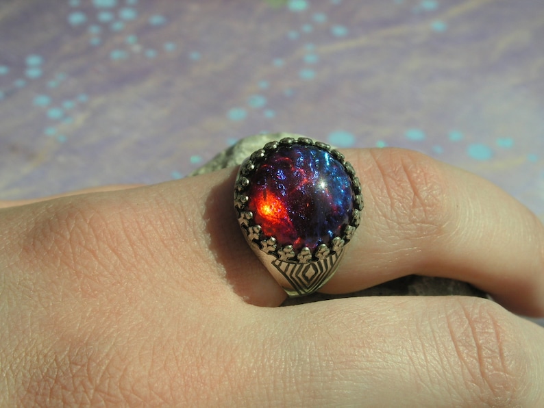 May include: A silver ring with a large, round, red and blue iridescent gemstone set in a decorative silver bezel.