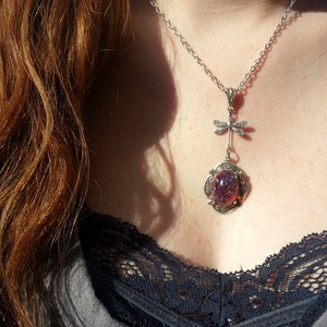 May include: A silver necklace with a dragonfly charm and a purple iridescent glass cabochon pendant.