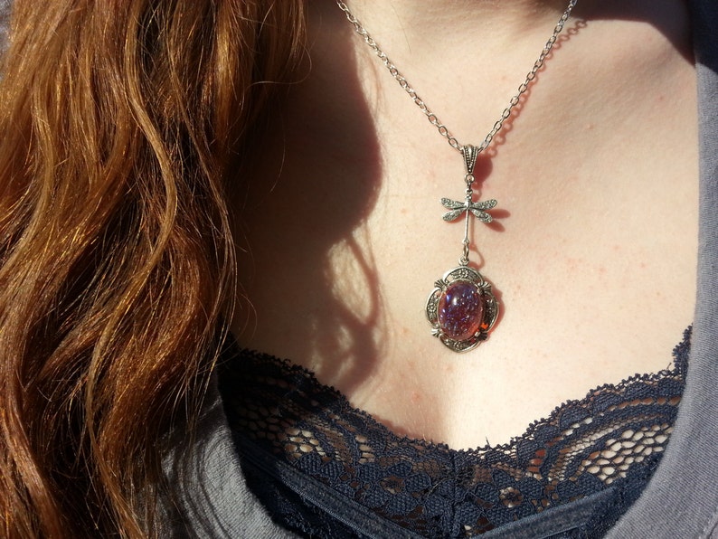May include: A silver necklace with a dragonfly charm and a purple iridescent glass cabochon pendant.