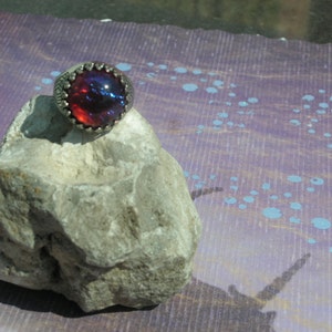 May include: A silver ring with a large, round, iridescent red and blue gemstone.