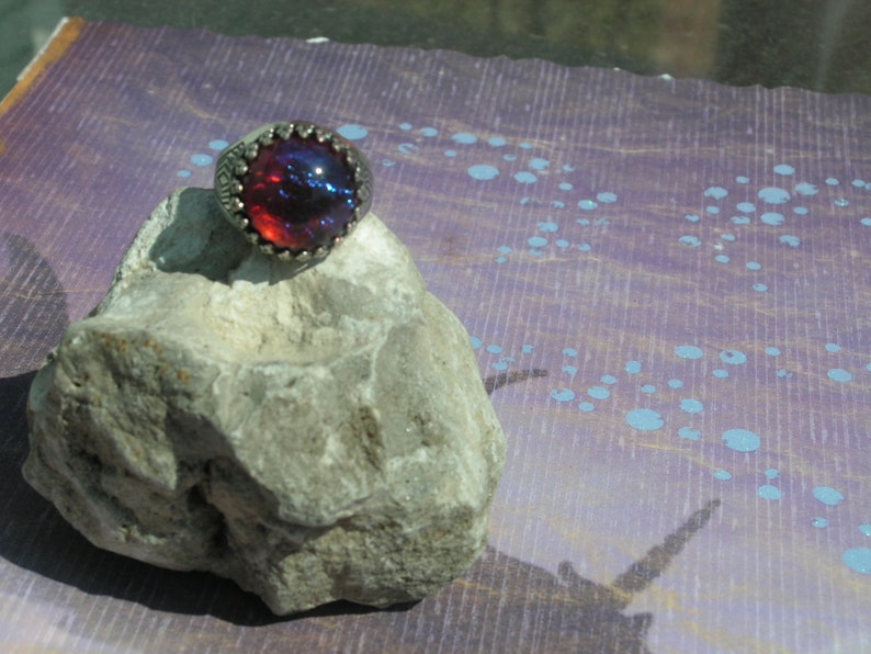 May include: A silver ring with a large, round, iridescent red and blue gemstone.
