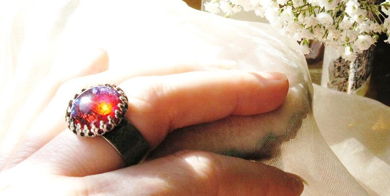 May include: A silver ring with a red and purple gemstone set in a decorative silver bezel. The ring is worn on a finger.