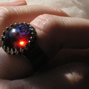 May include: A silver ring with a large, round, iridescent gemstone. The gemstone is a deep blue with red and purple hues.