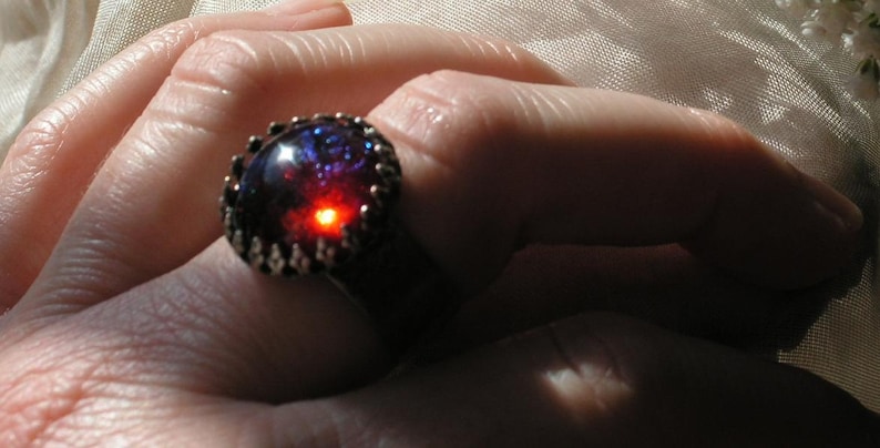 May include: A silver ring with a large, round, iridescent gemstone. The gemstone is a deep blue with red and purple hues.