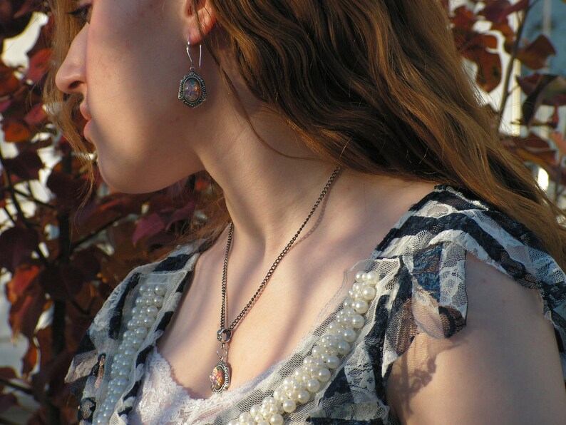 May include: A woman wearing a white and black lace top with a silver necklace and earrings. The necklace has a small pendant with a floral design.