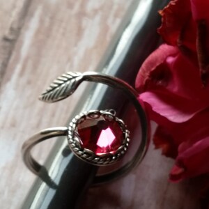 K&ouml;nnte beinhalten: Ein silberner Ring mit einem rosafarbenen Edelstein und einem Blattdesign. Der Ring liegt auf einer grauen Oberfl&auml;che.