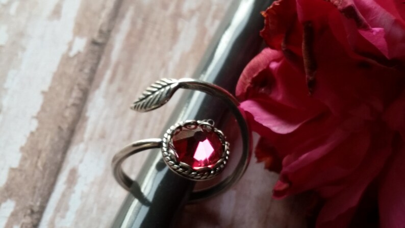 K&ouml;nnte beinhalten: Ein silberner Ring mit einem rosafarbenen Edelstein und einem Blattdesign. Der Ring liegt auf einer grauen Oberfl&auml;che.