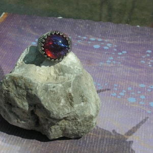 May include: A silver ring with a large, round, red and blue opal gemstone set in a decorative silver bezel.
