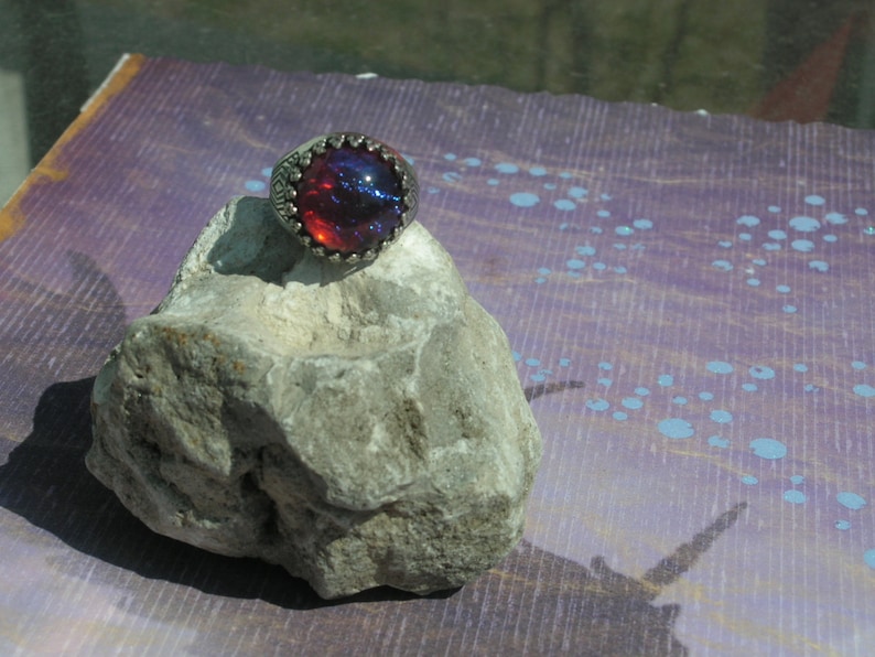 May include: A silver ring with a large, round, red and blue opal gemstone set in a decorative silver bezel.