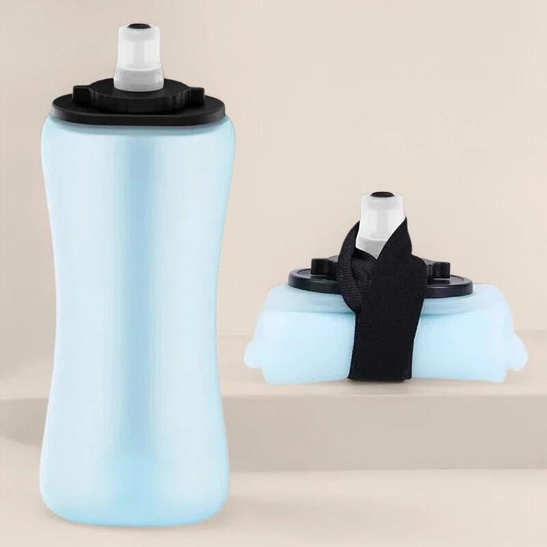 Puede incluir: Una botella de agua plegable de color azul claro con una tapa negra y una boquilla blanca. La botella se muestra tanto en posici&oacute;n vertical como plegada, con una correa negra para transportarla. La botella est&aacute; dise&ntilde;ada para un f&aacute;cil almacenamiento y portabilidad.