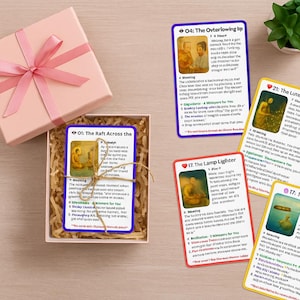 Puede incluir: Una caja de regalo rosa con una cinta, que contiene un juego de cartas de oráculo. Las cartas presentan ilustraciones y texto, con títulos como "The Raft Across the" y "The Lamp Lighter".