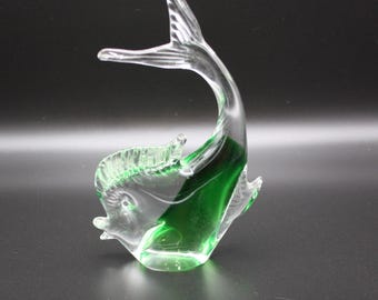 Könnte beinhalten: Eine klare Glasskulptur eines Fisches mit einer grünen Schwanzflosse. Der Fisch befindet sich in einer Sprunghaltung, wobei sein Schwanz über seinen Kopf gebogen ist.