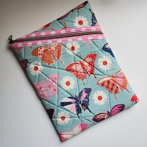 May include: Quilted zippered pouch featuring a butterfly and daisy pattern on a light blue background. The butterflies are in shades of red, orange, pink, and purple. The pouch has a pink zipper and a brown zipper pull.