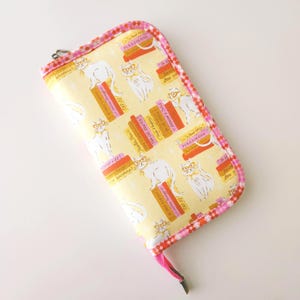 May include: A yellow zippered case with a repeating pattern of white cats wearing glasses and sitting on stacks of books. The books have titles like "Cat-22" and "Persuasion". The case is trimmed with pink and red fabric.