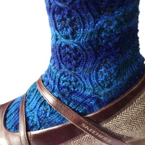 May include: Blue and teal knitted socks with a circular pattern. The socks are worn on a brown shoe with a brown strap.