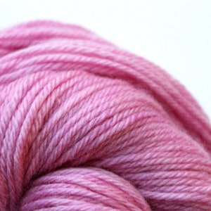 Op de afbeelding: Een close-up van een bol zachte, roze garen. Het garen is strak gewikkeld en heeft een subtiele glans.