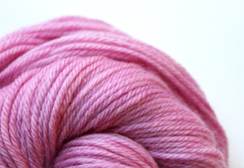 Op de afbeelding: Een close-up van een bol zachte, roze garen. Het garen is strak gewikkeld en heeft een subtiele glans.